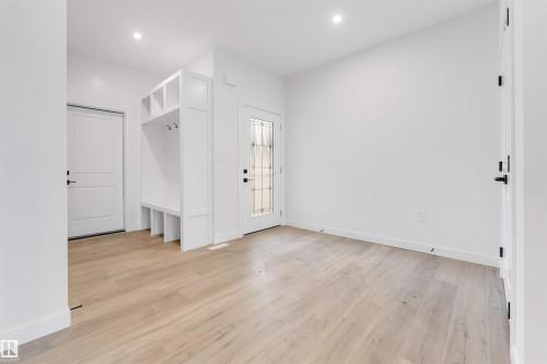 Inviting entryway featuring light wood-style flooring, a built-in white storage bench with hooks and cubbies, and a front door with decorative glass inserts - 22 Meadowgrove Landing, Spruce Grove, AB - Indoor Photo Showing Other Room