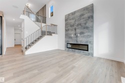 Spacious living area featuring light-toned flooring, a staircase with black metal railings, and a striking fireplace with a grey stone-like surround - 