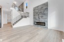 Spacious living area featuring light-toned flooring, a staircase with black metal railings, and a striking fireplace with a grey stone-like surround - 22 Meadowgrove Landing, Spruce Grove, AB  - Indoor With Fireplace 