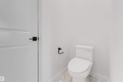 The bathroom features a modern toilet, white walls, and a white paneled door with matte black hardware - 
