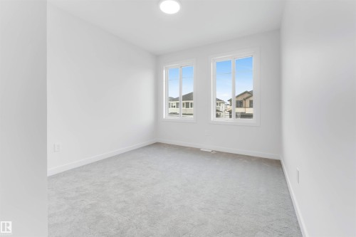 This room features light-colored walls, grey carpeting, and two windows providing views of the neighborhood - 22 Meadowgrove Landing, Spruce Grove, AB - Indoor Photo Showing Other Room