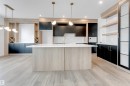 This kitchen features light-toned wood flooring, a central island with a white countertop, and dark cabinetry - 22 Meadowgrove Landing, Spruce Grove, AB  - Indoor Photo Showing Kitchen 