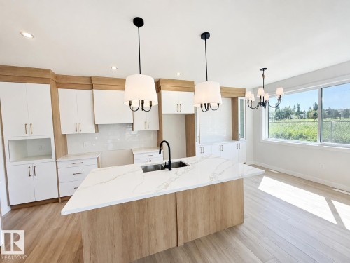 Expansive kitchen featuring a large central island, white cabinetry with wood-finish accents, quartz countertops, and integrated stainless steel sink with a matte black faucet - 22 Meadowgrove Landing, Spruce Grove, AB - Indoor Photo Showing Kitchen