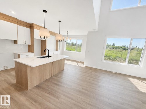Open-concept kitchen and living area featuring wood-finish flooring, a kitchen island with a dark basin sink, white cabinetry with wood-finish accents, and a high vaulted ceiling - 22 Meadowgrove Landing, Spruce Grove, AB - Indoor Photo Showing Kitchen