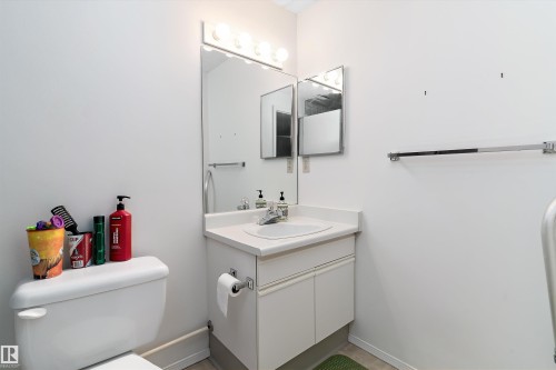 The bathroom features a toilet, a vanity with a white countertop and integrated sink, and a mirrored cabinet above the vanity - 5737 189 Street, Edmonton, AB - Indoor Photo Showing Bathroom