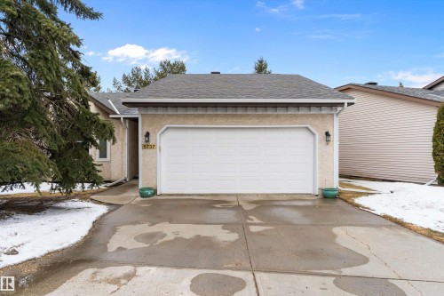 The property features an attached garage with a white garage door, exterior wall lanterns, and a paved driveway - 5737 189 Street, Edmonton, AB - Outdoor