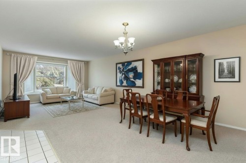 Well-lit living and dining area featuring neutral-toned carpet, a large window with drapes, and a chandelier - 5737 189 Street, Edmonton, AB - Indoor