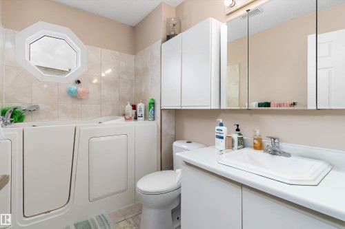 The bathroom features a walk-in bathtub, a vanity with an integrated sink, and an octagon-shaped window - 5737 189 Street, Edmonton, AB - Indoor Photo Showing Bathroom