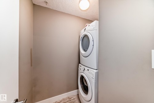Dedicated laundry area featuring a white stacked washer and dryer unit, and a ceiling-mounted light fixture - 506 11080 Ellerslie Road, Edmonton, AB - Indoor Photo Showing Laundry Room