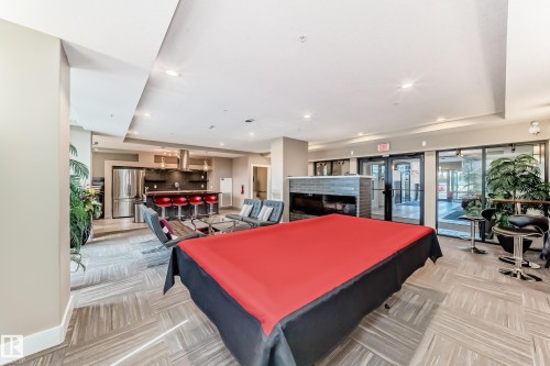 Spacious communal area featuring a kitchen with stainless steel appliances, a bar with seating, and a large table - 506 11080 Ellerslie Road, Edmonton, AB - Indoor Photo Showing Other Room