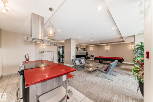 The property features an open-concept living area with tile flooring, a kitchen island with a red countertop, and a stainless steel range hood - 506 11080 Ellerslie Road, Edmonton, AB - Indoor Photo Showing Other Room