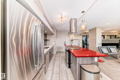 The kitchen features a stainless steel refrigerator, an island with a bright red countertop, and an overhead range hood - 506 11080 Ellerslie Road, Edmonton, AB - Indoor Photo Showing Kitchen With Stainless Steel Kitchen