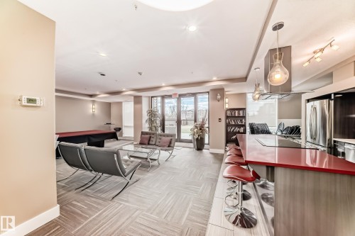 Spacious open-concept living area featuring a kitchen island with a red countertop, stainless steel appliances, and large windows - 506 11080 Ellerslie Road, Edmonton, AB - Indoor