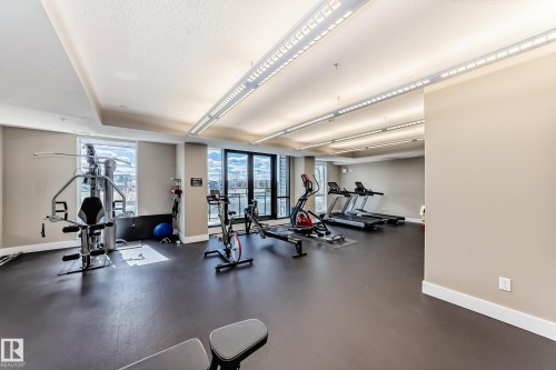 Fitness area featuring large windows, modern lighting fixtures, and dark flooring - 506 11080 Ellerslie Road, Edmonton, AB - Indoor Photo Showing Gym Room