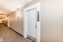 The property features a white entry door with a contemporary door number plaque, set in a neutral-toned hallway with wall-mounted lighting fixtures - 506 11080 Ellerslie Road, Edmonton, AB  - Indoor Photo Showing Other Room 