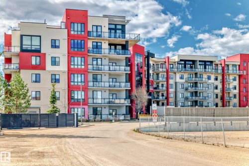 The property is an apartment complex featuring a modern exterior with red and beige facade panels, and glass balconies - 506 11080 Ellerslie Road, Edmonton, AB - Outdoor With Balcony With Facade