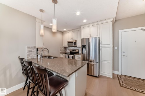 The kitchen features light-colored cabinetry, stainless steel appliances, and a central island with a sink and pendant lighting - 506 11080 Ellerslie Road, Edmonton, AB - Indoor Photo Showing Kitchen With Stainless Steel Kitchen With Double Sink With Upgraded Kitchen