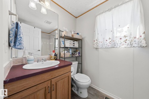 The bathroom features a vanity with a white oval sink set into a dark countertop, a mirror, and a wall-mounted light fixture - 66 Evergreen Park, Edmonton, AB - Indoor Photo Showing Bathroom