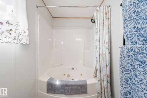 Bathroom featuring a corner jetted tub with an integrated shower, white paneled walls, and a white shower curtain with a floral pattern - 66 Evergreen Park, Edmonton, AB - Indoor Photo Showing Bathroom