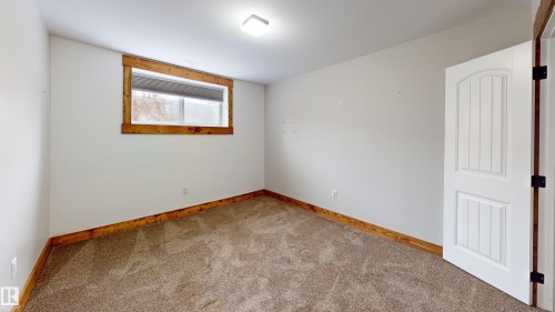 This room features light-colored walls, carpeted flooring, a window with a wood frame, and a white paneled door with dark hinges - 114039 Range Road 221, Rural Lethbridge County, AB - Indoor Photo Showing Other Room