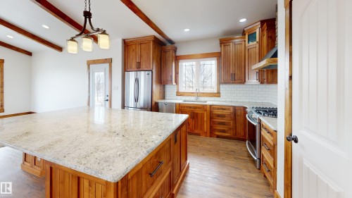 The kitchen features a large island with a light-colored granite countertop, wooden cabinetry, and stainless steel appliances - 114039 Range Road 221, Rural Lethbridge County, AB - Indoor Photo Showing Kitchen With Upgraded Kitchen