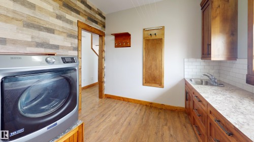 This utility room features wood plank flooring, a laundry appliance, and a sink with a white subway tile backsplash - 114039 Range Road 221, Rural Lethbridge County, AB - Indoor Photo Showing Laundry Room