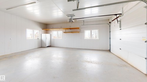 Spacious garage featuring white walls, multiple windows providing natural light, and overhead shelving for storage - 114039 Range Road 221, Rural Lethbridge County, AB - Indoor Photo Showing Garage