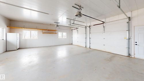 This spacious garage features a light-colored concrete floor, three garage doors, and a side entry door - 114039 Range Road 221, Rural Lethbridge County, AB - Indoor Photo Showing Garage