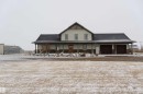 This property features a covered porch, a two-car garage with individual doors, and a light-colored exterior with stone accents - 114039 Range Road 221, Rural Lethbridge County, AB  - Outdoor 