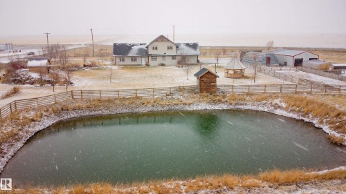 The property features a large pond, a two-story home, and several outbuildings, all surrounded by a fenced perimeter - 114039 Range Road 221, Rural Lethbridge County, AB - Outdoor With Body Of Water With View