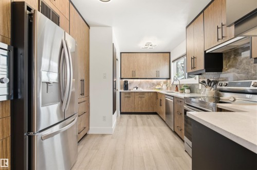 The kitchen features wood cabinetry with black hardware, stainless steel appliances, light-colored countertops, and a window providing natural light - 12904 95 Street, Edmonton, AB - Indoor Photo Showing Kitchen With Double Sink
