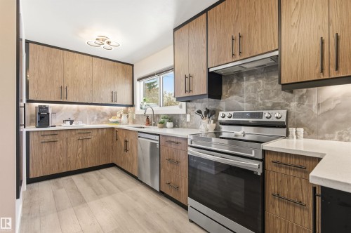 Modern kitchen featuring wood-grain cabinetry, stainless steel appliances, a window providing natural light, and a stylish backsplash - 12904 95 Street, Edmonton, AB - Indoor Photo Showing Kitchen