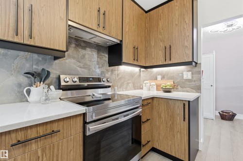 The kitchen features wood cabinetry with black hardware, stainless steel appliances, a grey tiled backsplash, and white countertops - 12904 95 Street, Edmonton, AB - Indoor Photo Showing Kitchen