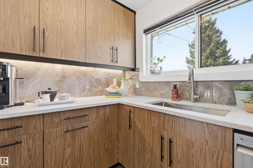 The kitchen features wood grain cabinetry with black hardware, white countertops, and a grey tile backsplash - 12904 95 Street, Edmonton, AB - Indoor Photo Showing Kitchen