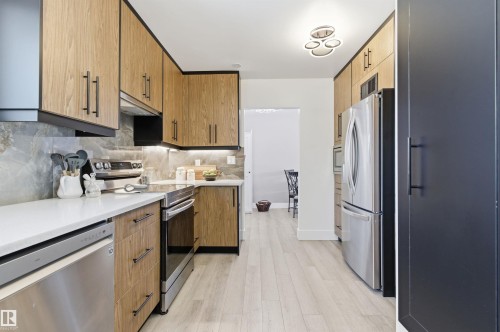 The kitchen features wood-look cabinetry with dark hardware, stainless steel appliances, and light countertops - 12904 95 Street, Edmonton, AB - Indoor Photo Showing Kitchen