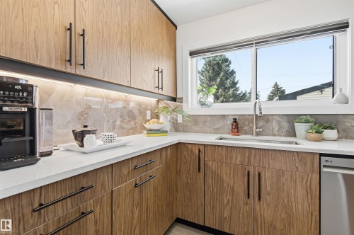 The kitchen features wood grain cabinetry with black handles, light countertops, and a tile backsplash - 12904 95 Street, Edmonton, AB - Indoor Photo Showing Kitchen