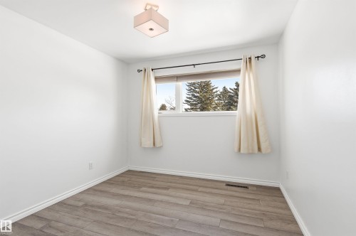 This room features light-colored walls, wood-look flooring, and a window with a view of trees - 12904 95 Street, Edmonton, AB - Indoor Photo Showing Other Room