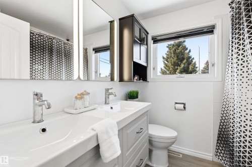 The bathroom features a double vanity with chrome faucets, a lighted mirror, and a window providing natural light - 12904 95 Street, Edmonton, AB - Indoor Photo Showing Bathroom