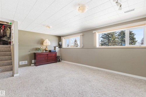 This spacious room features light-colored carpeting, multiple windows providing natural light, and a functional staircase - 12904 95 Street, Edmonton, AB - Indoor