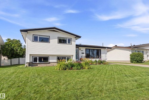 The property features a well-maintained lawn and a flower bed with varied plantings, complementing the white exterior siding and dark trim - 12904 95 Street, Edmonton, AB - Outdoor