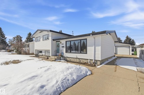 The property features a white exterior with dark trim windows, a front entrance with a light blue door, and a concrete driveway leading to a garage - 12904 95 Street, Edmonton, AB - Outdoor