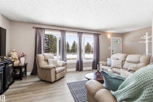 The living area features light-colored walls, light wood-style flooring, and large windows with dark curtains - 12904 95 Street, Edmonton, AB - Indoor Photo Showing Living Room