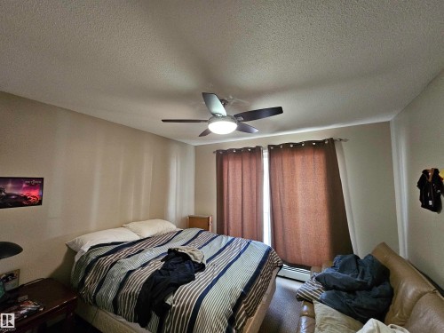The room features a ceiling fan with integrated lighting, a window with curtains, and neutral-toned walls - 8 10616 123 Street, Edmonton, AB - Indoor Photo Showing Bedroom