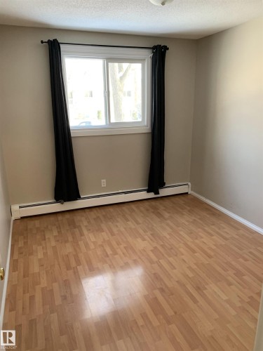 Room featuring wood-finish flooring, a double window with white trim, and light beige wall paint - 8 10616 123 Street, Edmonton, AB - Indoor Photo Showing Other Room