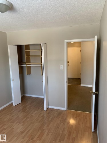 Room featuring wood-finish flooring, neutral wall paint, and a built-in closet with bifold doors and shelving - 8 10616 123 Street, Edmonton, AB - Indoor Photo Showing Other Room