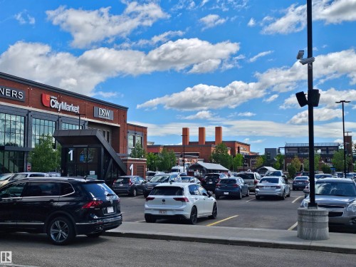 The property is located within a commercial area featuring a retail building with large windows and a red brick facade - 8 10616 123 Street, Edmonton, AB - Outdoor With View