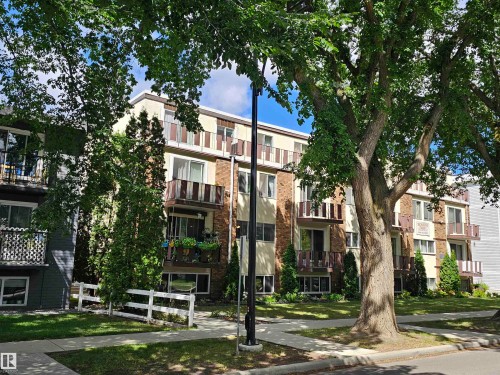 The property features a multi-story exterior with balconies, set amidst mature trees and a manicured lawn - 8 10616 123 Street, Edmonton, AB - Outdoor