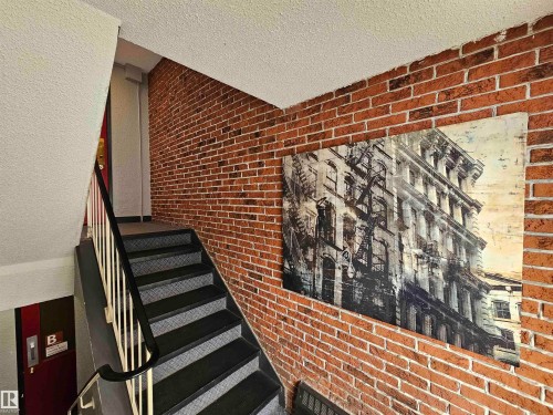 The property features a staircase with a black handrail and white balusters, set against a brick-patterned wall - 8 10616 123 Street, Edmonton, AB -  Photo Showing Other Room