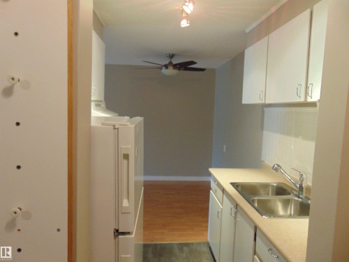 Kitchen featuring white cabinetry, a double-basin stainless steel sink, and a white tile backsplash - 8 10616 123 Street, Edmonton, AB - Indoor Photo Showing Kitchen With Double Sink