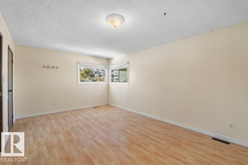 This room features light-toned flooring, windows providing views of exterior trees, and a ceiling light fixture - 17313 60 Avenue, Edmonton, AB - Indoor Photo Showing Other Room